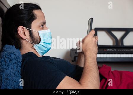 Young latin man using face mask sick on bed at home using the phone Stock Photo