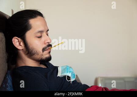 Young latin man sick on bed at home with a thermometer in his mouth Stock Photo