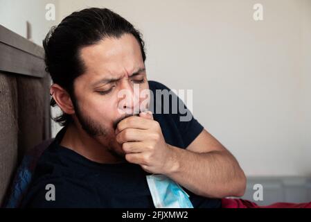 Young latin man sick on bed at home coughing Stock Photo