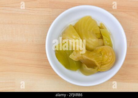 Pickled mustard green in brine, preserved vegetable in salted water in white bowl on wooden background, top view Stock Photo