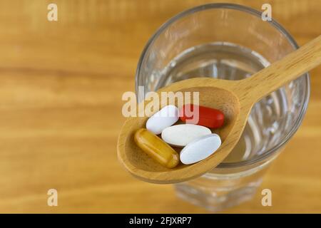 Dietary supplements in wooden spoon, royal Jelly in soft gel capsule, film coated tablets of Multi Vitamins and Minerals on glass of water with wood b Stock Photo