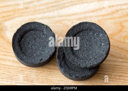 Black round disc of Arabian charcoals to burn aromatic incense, resin gum, free of chemical additives on wood background Stock Photo