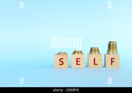 Increasing stack of coins with word self on wooden blocks in blue background. Invest on yourself improvement concept. Stock Photo