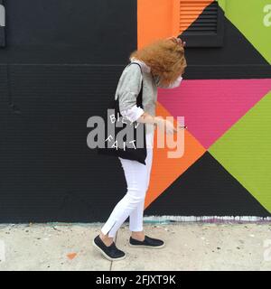 Woman walking down the streets of Wynwood wearing Madewell clothing and a Madewell purse that reads Bein Fait. Stock Photo