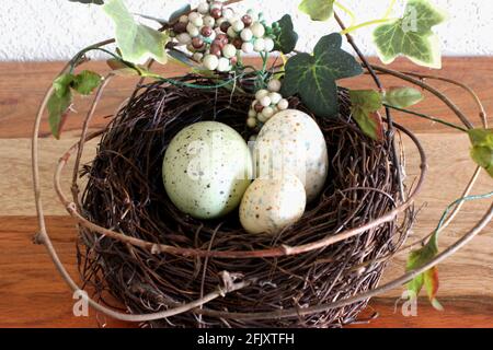 Spring illustration. 3 small colored eggs in a pine nest for Easter time, green leaves and twigs all around on wooden table, closeup Stock Photo