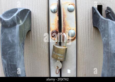 An outdoor storage house, shed, closeup of a master lock with key inserted and broken scratched door handles. The lock area is rusted and old. Stock Photo