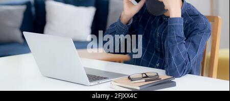 Young asian business man in face mask talking smartphone and work on laptop computer for protect covid-19, businessman quarantine work from home with Stock Photo