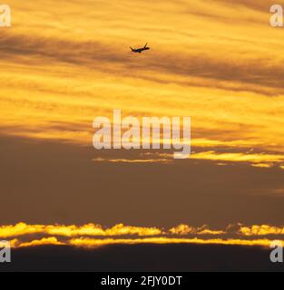 Wimbledon, London, UK. 27 April 2021. An early arrival to London Heathrow airport begins the descent against a colourful backdrop of early clouds at sunrise. Credit: Malcolm Park/Alamy Live News.