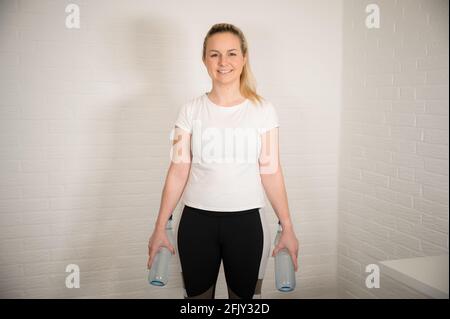 Happy blonde woman doing fitness exercise with water bottles - basic sport workout as a training at home Stock Photo