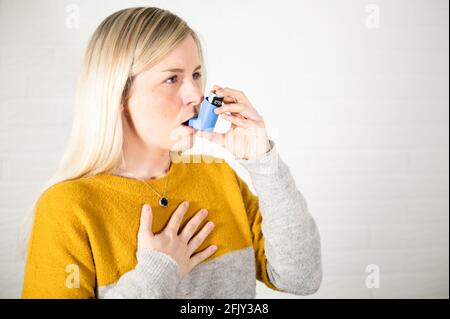 Young blonde woman holding an asthma spray inhaler in her hand Stock Photo