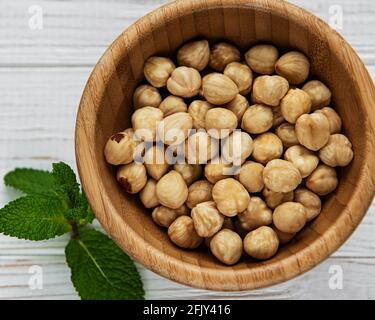 Peeled hazelnuts in a bowl on white wooden background Stock Photo