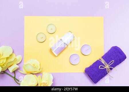 Scented candles, towel,  lotion and orchid flowers on a yellow and purple background. Top view, copy space. Spa concept, flat lay. Stock Photo