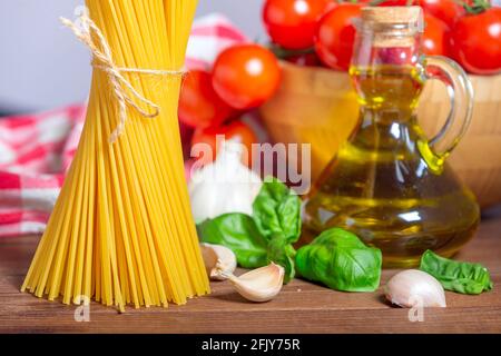 Italian food ingredients for cooking Spaghetti, Pasta. Raw spaghetti pasta with various ingredient - tomatoes, garlic, basil, and oil on wood backgrou Stock Photo
