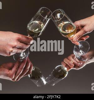 A female and a male hand holding flute glasses with sparkling wine toast on a reflective mirror surface Stock Photo