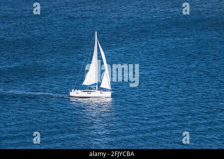 aerial view of a generic white sailboat with two sails sailing on very calm water in the San Diego Bay in Southern California Stock Photo