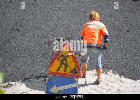 Road street repairing works. Female worker during asphalting road. Heavy female manual labor in construction Stock Photo