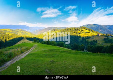 rural landscape in mountains at summer sunrise. country road through grassy pasture winding down in to the distant valley. clouds on the blue sky abov Stock Photo
