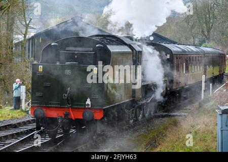 Historic heritage steam train or loco puffing clouds of smoke (enthusiast taking photo by tracks) - Oxenhope Station sidings, Yorkshire, England, UK. Stock Photo