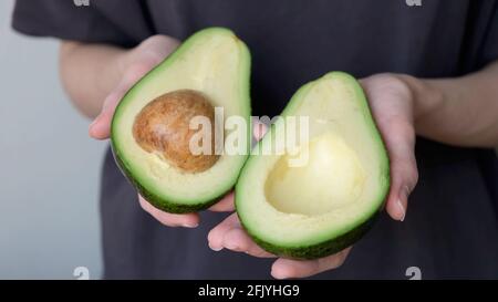 Avocado halves in female hands. Healthy food, tropical fruit Avocado Stock Photo