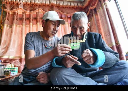 (210427) -- LHASA, April 27, 2021 (Xinhua) -- Lhapu (R) listens to his son's explanation to the medical insurance card at Lin'a Village of Dagze County in Lhasa, southwest China's Tibet Autonomous Region, April 25, 2021.  Lhapu, born in 1938, worked as a serf before the democratic reform in Tibet in 1959, which abolished its feudal serfdom under theocracy. 'As part of the production tools, we just did what the lord asked us to do, and were even forbidden to speak loudly,' Lhapu recalled his life in the old times, adding that children had no guaranteed food and clothing. After the democratic re Stock Photo