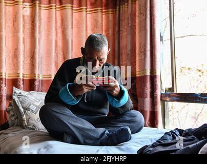 (210427) -- LHASA, April 27, 2021 (Xinhua) -- Lhapu listens to the radio at home at Lin'a Village of Dagze County in Lhasa, southwest China's Tibet Autonomous Region, April 25, 2021. Lhapu, born in 1938, worked as a serf before the democratic reform in Tibet in 1959, which abolished its feudal serfdom under theocracy. 'As part of the production tools, we just did what the lord asked us to do, and were even forbidden to speak loudly,' Lhapu recalled his life in the old times, adding that children had no guaranteed food and clothing. After the democratic reform, great changes have taken place i Stock Photo