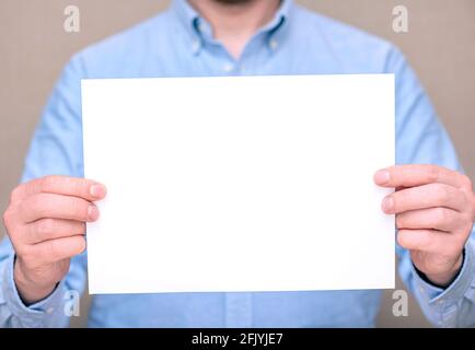 A man in blue shirt, businessman holding white blank sheet. Space for text, mockup Stock Photo