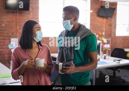 Diverse business colleagues wearing face masks having coffee in office Stock Photo
