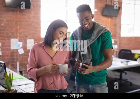 Diverse business colleagues having coffee in office and looking at smartphone Stock Photo