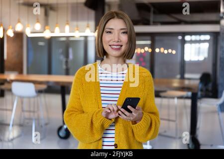 Portrait of asian smiling businesswoman standing holding and using a smartphone Stock Photo