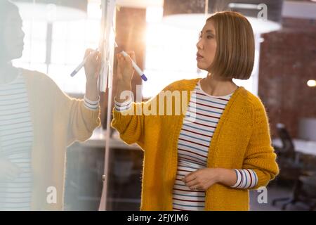 Portrait of asian businesswoman standing in front of glass wall and writing Stock Photo
