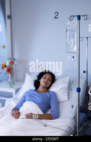 Mixed race female patient lying asleep in hospital bed wearing fingertip pulse oximeter and iv drip