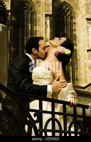 Gorgeous wedding couple (bride and groom) standing in front of historical church building and kissing. Stock Photo