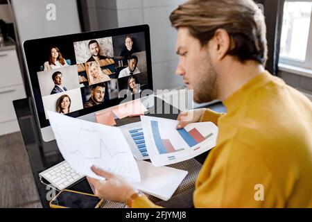 Concentrated male employee in yellow shirt working from home, having online briefing meeting with colleagues. Serious young businessman doing Stock Photo