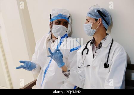 Medical workers in protective costumes, gloves, and masks sitting and discussing something Stock Photo