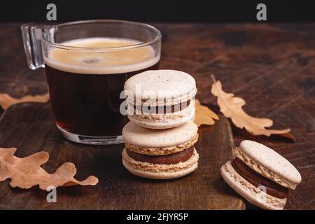 Cup of coffee and chocolate macarons on wooden background. Cozy autumn composition. Hot espresso in a glass cup - Image Stock Photo