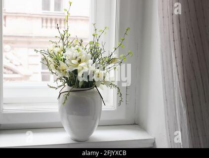 Easter spring still life. Floral bouquet on window sill. White and yellow tulips, daffodils flowers and green birch tree and blueberry branches in Stock Photo