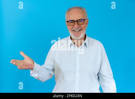 Grey haired senior man wearing casual shirt standing over blue background smiling cheerful presenting and pointing with palm of hand looking at the ca Stock Photo