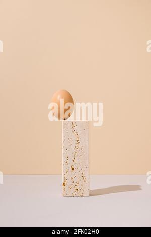 Single egg standing on a travertine marble block on a beige and gray background. 2021 Easter unique surreal still life arrangement. Stock Photo