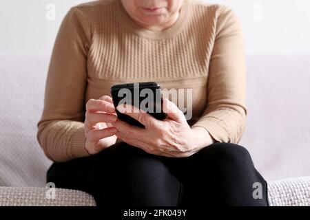 Elderly woman with smartphone sitting on sofa at home, mobile phone in female hands. Concept of online communication in retirement, sms, social media Stock Photo
