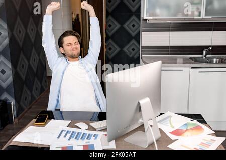 Stylish male employee sitting at the desk in home office, stretching. Caucasian young adult businessman takes a little break from work, resting after Stock Photo
