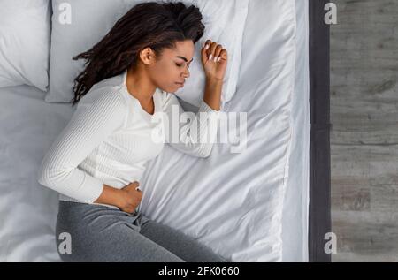 Stomachache Concept. Above Top View Of Sad Black Woman Touching Aching Abdomen Having Stomach Pain. Food Poisoning, Gastritis, Period Cramps And Abdom Stock Photo