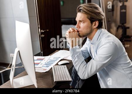 Pensive male freelancer developing new project, sitting at the desk in home office. Stylish young businessman or student is working or studying Stock Photo