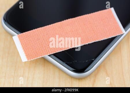 Extra strong fabric plaster on broken smart phone with cracked screen, on wooden background, soft focus Stock Photo