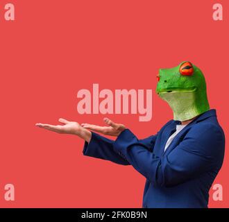 man with googly-eyed frog mask looking pointing and holding with both hands on red background with copy space Stock Photo