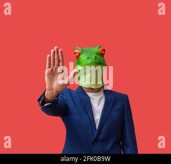 man in a frog mask with bulging eyes pointing to stop with his hand and indicating to stop as if he were a policeman on a red background with copy spa Stock Photo