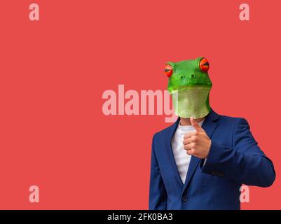 man with googly-eyed frog mask making a like or thumbs-up on red background with copy space Stock Photo