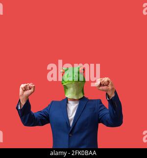 man with googly-eyed frog mask euphoric with arms in the air celebrating on red background with copy space Stock Photo
