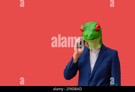 man with googly-eyed frog mask calling with smart phone on red background with copy space Stock Photo