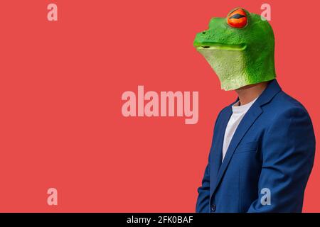 man in frog mask with bulging eyes staring and posing on red background with copy space Stock Photo