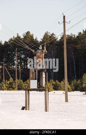 An impressive winter evening in nature, a transformer box in the field. The concept of power grids in the countryside. In the background there is a forest in the evening sunlight. Stock Photo